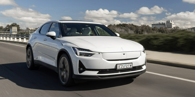 Front view of a white Polestar 2 travelling along a road on a sunny day.